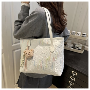 Detail of white tote bag featuring colorful embroidery and cute brown plush bear charm