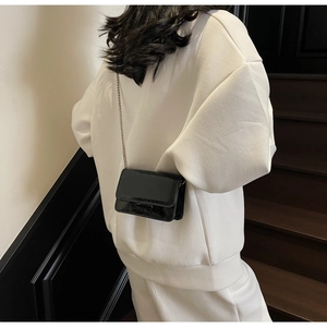 Detail view of black patent leather crossbody bag with chain strap on white outfit