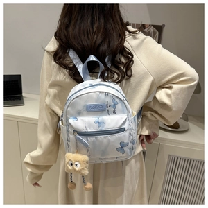 Rear view of light blue mini backpack with butterfly print and plush charm on model