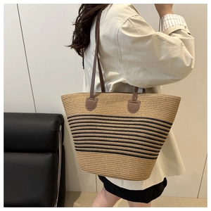 Detail of woven straw tote bag with dark stripes and brown leather shoulder strap