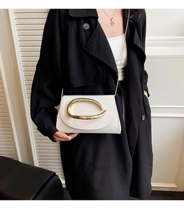 Detail of white leather shoulder bag featuring a large gold metallic loop and fine chain