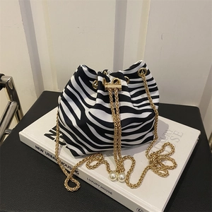 Close-up of zebra pattern bucket bag with gold chain and pearl pendants on book