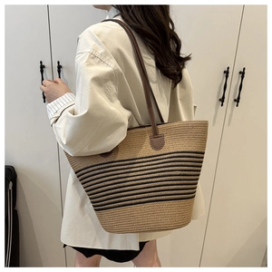 Detail view of large woven straw tote bag with black stripes and brown leather straps