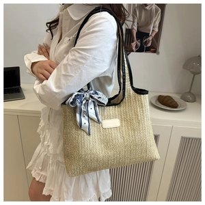 Detail of woven straw tote bag with black leather straps and decorative Paris scarf