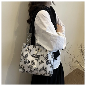 Detail of grey fabric shoulder bag with butterfly prints and metal chain strap