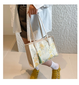 Detail shot of a cream tote bag featuring intricate yellow floral embroidery and green tassel