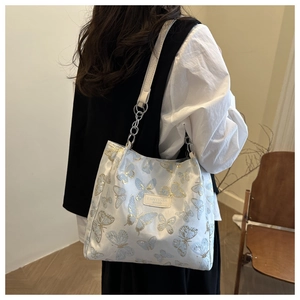 Detail of white shoulder bag featuring exquisite blue and gold butterfly embroidery and chain strap