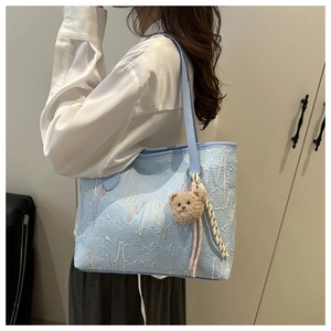 Detail of light blue tote bag featuring wave embroidery and a cute brown bear charm