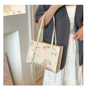 Detail view of a beige tote bag with floral embroidery and a green tassel charm accessory