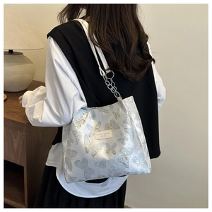 Detail of white tote bag featuring blue butterfly jacquard and silver chain leather strap