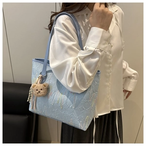Detail of light blue tote with wave embroidery and cute plush bear charm on the strap