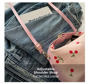 Close-up of pink corduroy bag with cherry embroidery and adjustable gold metal buckle
