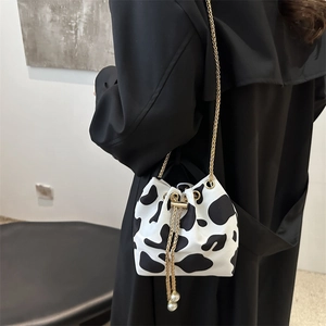 Detail of cow print bucket bag with gold chain strap and pearl tassels on a model