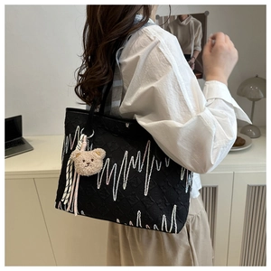 Detail of black tote bag with wave embroidery and brown plush bear charm accessory