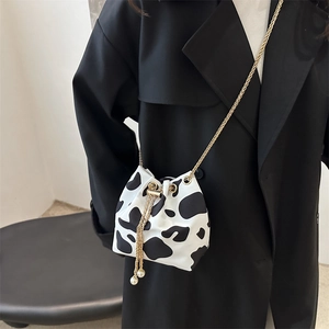 Detail of cow print bucket bag with gold chain and pearl tassels on a black trench coat