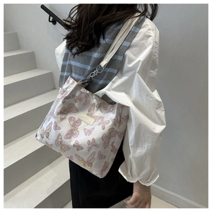Detail of white tote bag featuring pink butterfly prints and silver chain strap on model