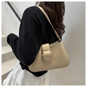 Beige shoulder bag with gold square buckle shown on model in a minimalist setting
