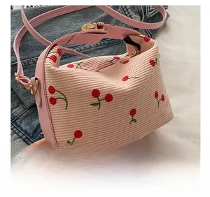 Detail of pink corduroy shoulder bag featuring cherry embroidery and gold hardware