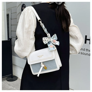 Detail of a chic cream crossbody bag with floral silk scarf knot on the shoulder strap