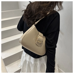 Detail of beige underarm bag with gold buckle on a model in a minimalist outdoor setting