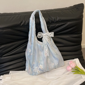 Sac fourre-tout bleu clair brodé avec nœud en dentelle et motif floral sur canapé en cuir