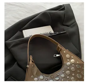 Close-up of tan crescent underarm bag with silver stud details on a grey blazer