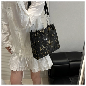Detail of black tote bag featuring golden butterfly patterns and metallic chain straps