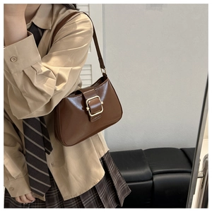 Detail of vintage brown glossy leather shoulder bag with a gold buckle worn by a model