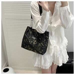 Detail of black crossbody bag with gold butterfly prints and metal chain strap