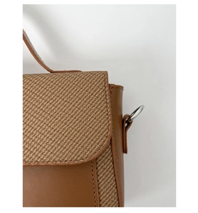 Detail view of brown textured fabric flap and smooth leather bag with silver metal ring