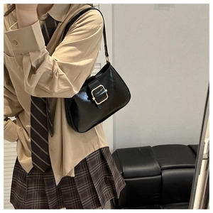 Close-up of a black glossy shoulder bag with a prominent golden square metal buckle detail