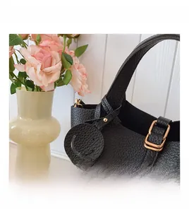Detail of black lychee grain leather bucket bag with gold hardware and smiley face charm