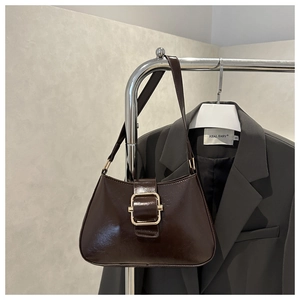 Detail of glossy dark brown leather shoulder bag with decorative large gold metal buckle