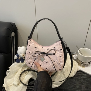 Sac à main plissé rose avec broderie nœud noir et pendentif cœur sur une table de café