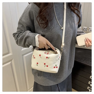 Detail of white corduroy crossbody bag featuring red cherry embroidery and gold hardware