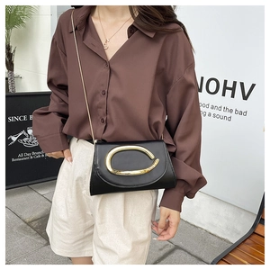 Detail of a black leather crossbody bag with a large gold C-shaped metal buckle on the flap