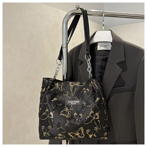 Detail of black tote bag with golden butterfly embroidery and metal chain strap
