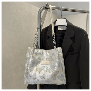 Close-up of white tote bag featuring blue and gold butterfly embroidery and chain strap