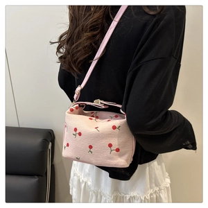 Pink crossbody bag with red cherry embroidery on textured corduroy shown on a model