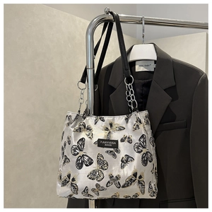Detail of elegant butterfly embroidery and metallic chain strap on white tote bag