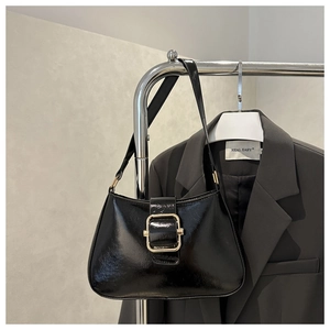 Glossy black underarm bag with gold square buckle shown on a metal stand for styling