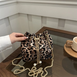 Fashionable leopard print bucket bag with gold chain strap and pearl charm on a wooden table