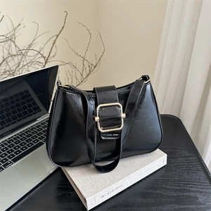 French style black glossy leather underarm bag with gold buckle on a book