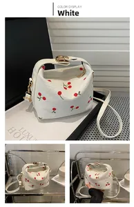 Detail of white textured shoulder bag with red cherry embroidery and gold metal twist lock