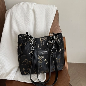 Black tote bag featuring gold butterfly embroidery and a chain strap on a wooden chair