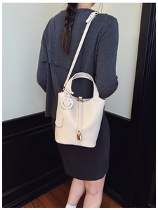 Detail view of white pebbled leather bucket bag with gold padlock and smiley pendant