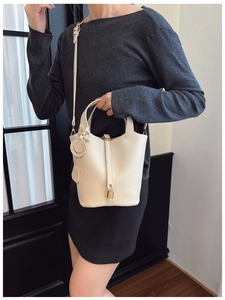 Detail of creamy white pebble leather bucket bag with gold clasp and leather charm