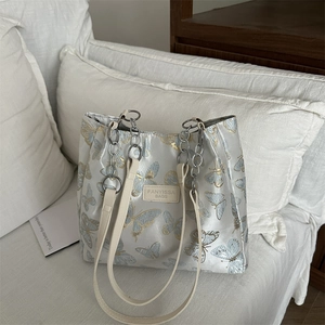 Silver silk tote bag with butterfly embroidery and metal chain on white sofa