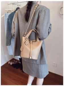Detail of beige lychee pattern bucket bag with metal padlock and cute leather charm