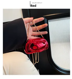 Detail of red metallic mini bag with oval relief and gold chain strap held by hand